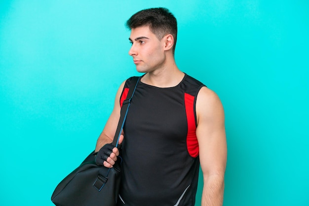 Giovane uomo sportivo caucasico con borsa sportiva isolata su sfondo blu che guarda al lato