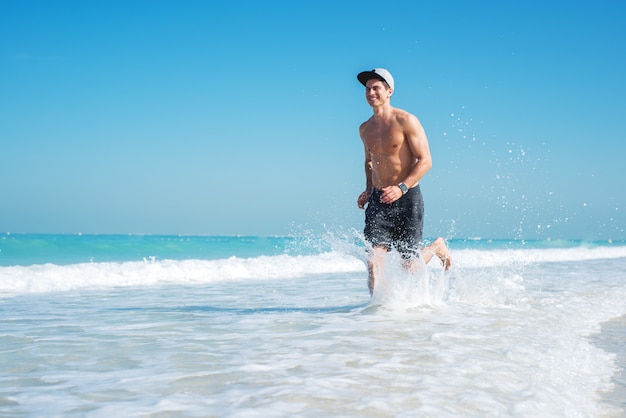 Giovane uomo sportivo che corre lungo la bellissima spiaggia, cercando felice.