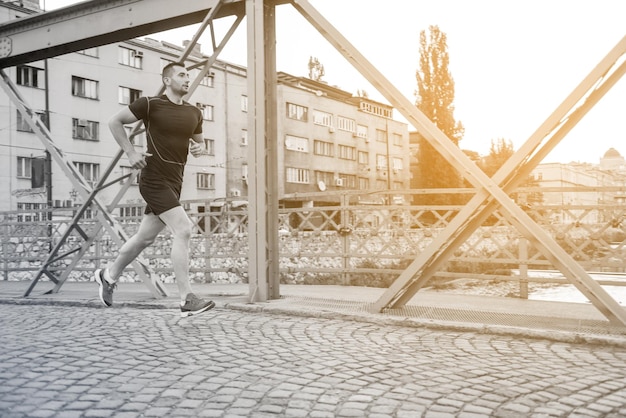 giovane uomo sportivo che fa jogging attraverso il ponte al mattino soleggiato della città