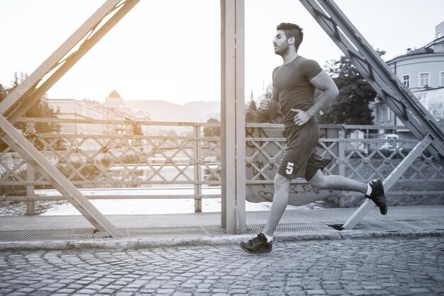 giovane uomo sportivo che fa jogging attraverso il ponte al mattino soleggiato della città