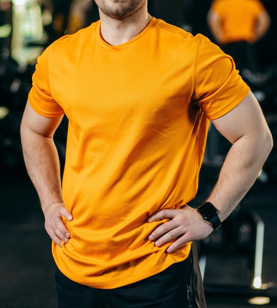 Giovane uomo sportivo in maglietta arancione in palestra da vicino