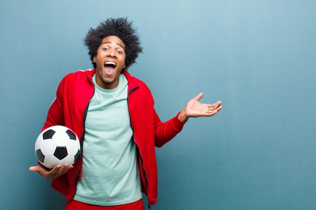 Giovane uomo sportivo nero con un pallone da calcio contro il wa blu del grunge