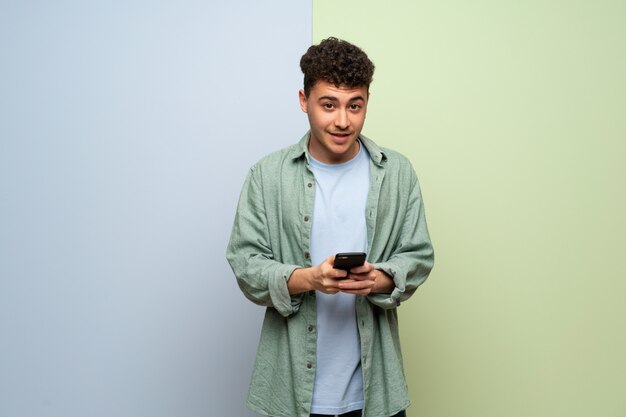 Giovane uomo su sfondo blu e verde inviando un messaggio con il cellulare