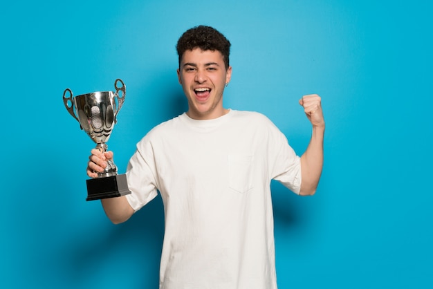 Giovane uomo su sfondo blu in possesso di un trofeo