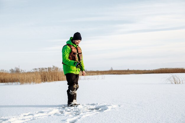 Giovane uomo su una battuta di pesca invernale su un lago innevato pesci su una canna da pesca