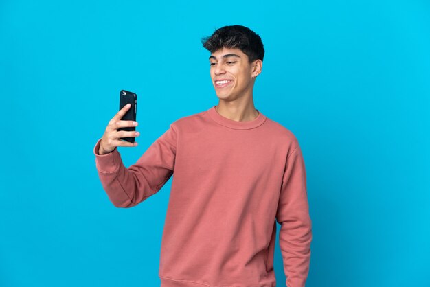 Giovane uomo sul blu isolato facendo un selfie