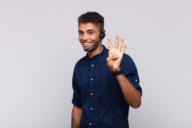 Giovane uomo telemarketer sorridente e guardando amichevole, mostrando il numero quattro o quarto con la mano in avanti, conto alla rovescia