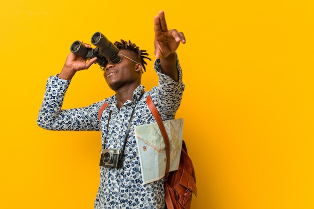 Giovane uomo turistico africano che sta contro un fondo giallo che tiene un binocolo