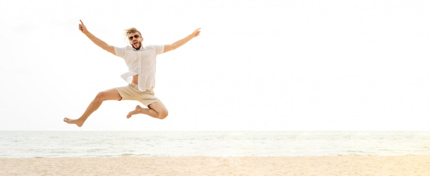 Giovane uomo turistico felice energico che salta in spiaggia