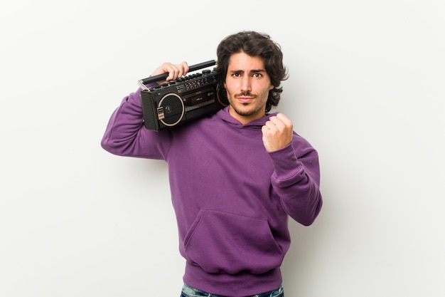 Giovane uomo urbano che tiene un guetto blaster che mostra il pugno alla macchina fotografica, espressione facciale aggressiva.