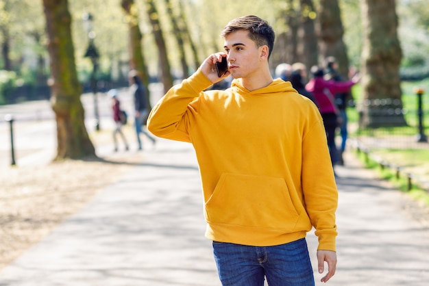 Giovane uomo urbano che utilizza smartphone che cammina nella via in un parco urbano a Londra.