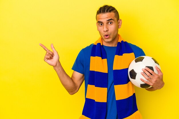 Giovane uomo venezuelano che guarda il calcio isolato su sfondo giallo che punta al lato