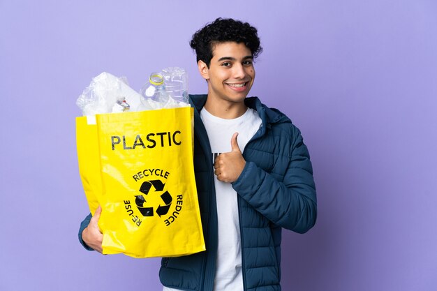 Giovane uomo venezuelano che tiene una borsa piena di bottiglie di plastica che danno un pollice in alto gesto