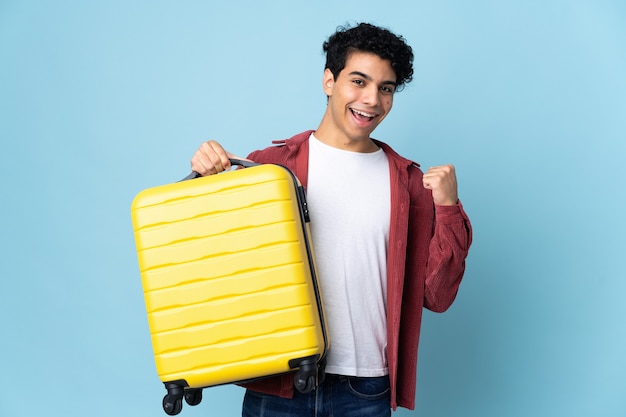 Giovane uomo venezuelano isolato su sfondo blu in vacanza con la valigia da viaggio