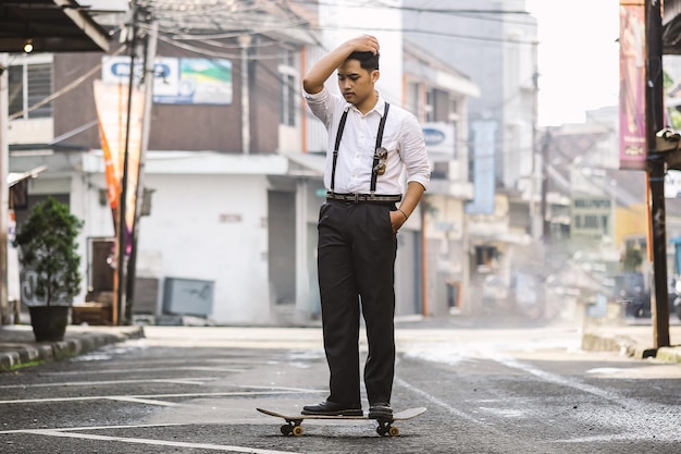 Giovane uomo vestito con un abito elegante in sella a uno skateboard per la strada della città