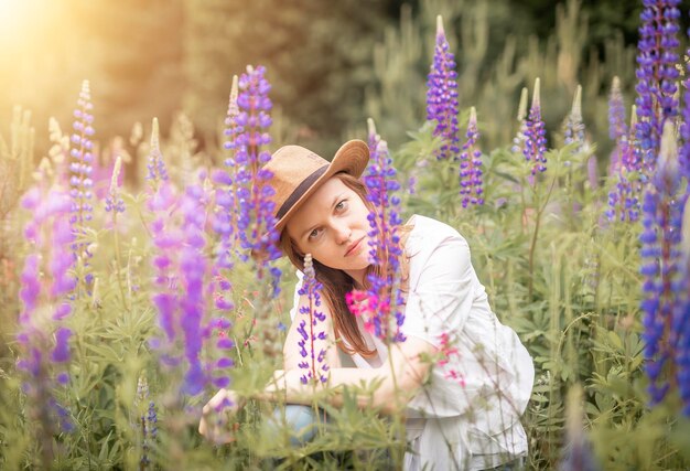 Giovane vera donna con cappello di paglia seduta in un campo di fiori di lupino in estate