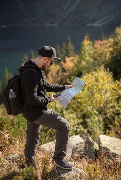 Giovane viaggiatore con mappa e zaino rilassante all'aperto con montagne rocciose sullo sfondo