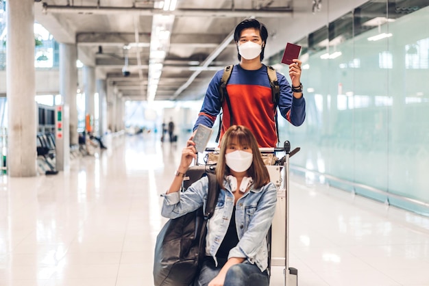 Giovane viaggiatore di coppia felice in quarantena per coronavirus che indossa una maschera chirurgica per la protezione del viso tenere passaporto e biglietto prima del volo di lunga vacanza al terminal internazionale dell'aeroporto