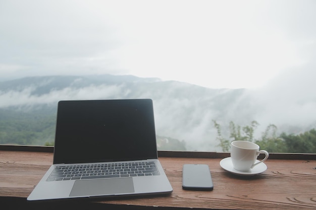 Giovane viaggiatore freelance che indossa un cappello ovunque lavora online utilizzando il laptop e si gode la vista sulle montagne