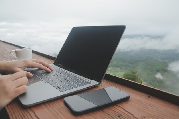 Giovane viaggiatore freelance che indossa un cappello ovunque lavora online utilizzando il laptop e si gode la vista sulle montagne