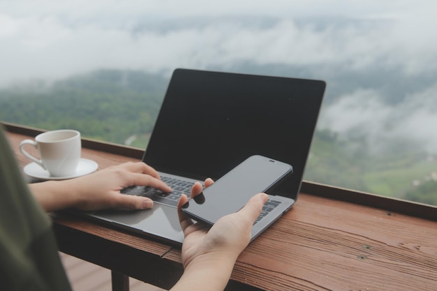 Giovane viaggiatore freelance che indossa un cappello ovunque lavora online utilizzando il laptop e si gode la vista sulle montagne