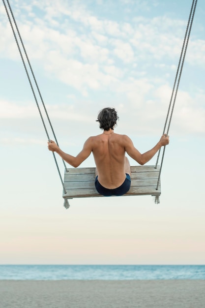 Giovane viaggiatore godendo le sue vacanze estive sull'altalena in riva al mare Oscillazione sulla spiaggia Vista posteriore