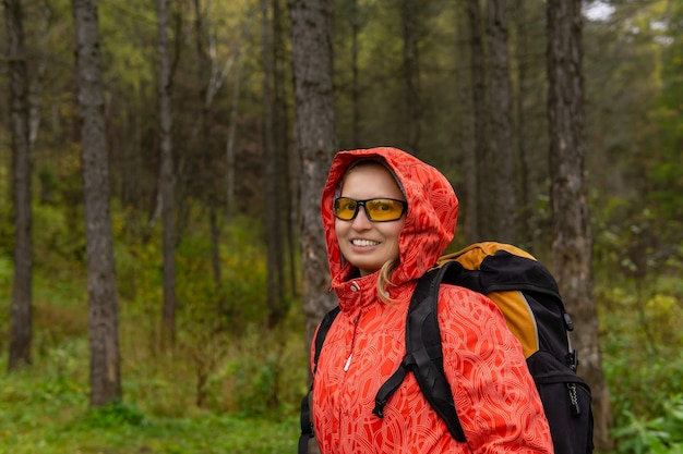 Giovane viaggiatrice bionda con zaino nella foresta autunnale