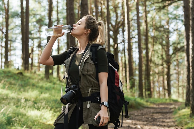 Giovane viandante femminile che beve acqua dalla bottiglia riutilizzabile nella foresta verde