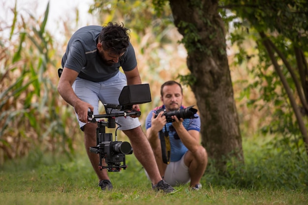 giovane videografo con gimball video slr rocording mentre una donna sana fa esercizio di yoga nella bellissima natura sulla riva del fiume