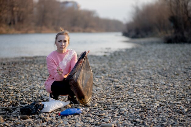 Giovane volontaria femminile che raccoglie immondizia sul fiume