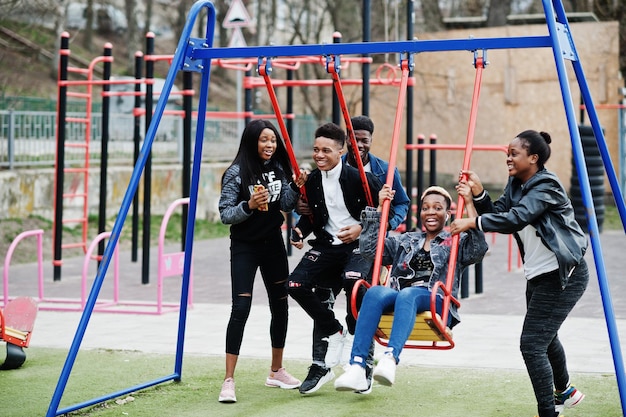 Giovani amici africani millennial sul parco giochi scivolano e oscillano Felici i neri che si divertono insieme Concetto di amicizia della Generazione Z