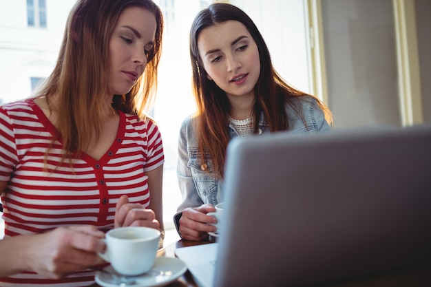 Giovani amici che per mezzo del computer portatile al caffè