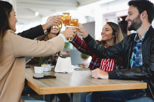 Giovani amici che si divertono a tifare con la birra all'interno del bar ristorante - Focus sulla mano destra della ragazza