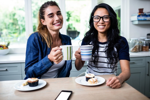 Giovani amici femminili che tengono la tazza di caffè durante la prima colazione