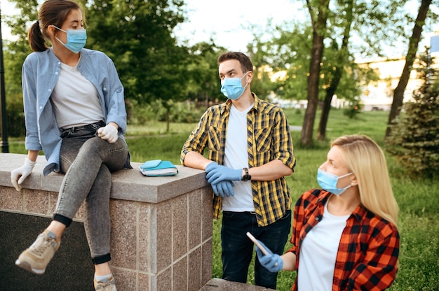 Giovani amici in maschere e guanti svaghi nel parco, quarantena. Persona di sesso femminile che cammina durante l'epidemia, assistenza sanitaria e protezione, stile di vita pandemico