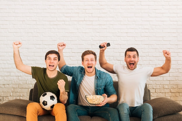 Giovani amici maschi che incoraggiano mentre guardano la partita di calcio sulla televisione