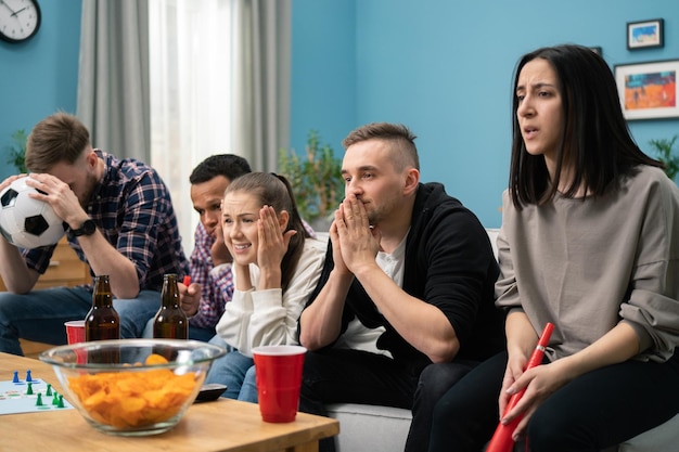 Giovani amici multirazziali che guardano la partita di calcio in tv insieme a casa e delusi dalla loro