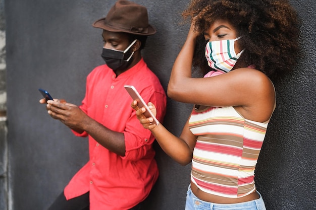 Giovani amici neri che usano il cellulare mentre indossano una maschera protettiva per il viso durante l'epidemia di coronavirus - Focus on girl face