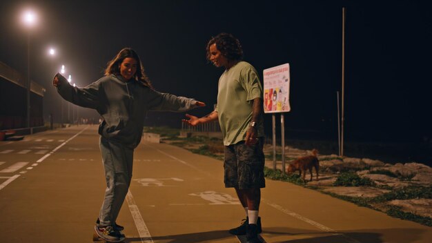 Giovani attivi che si allenano a fare longboard di notte, pattinatori di strada, coppia che si baciano.