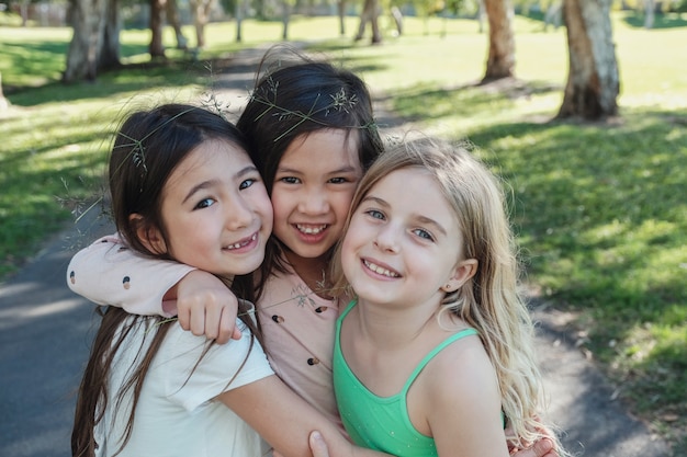 Giovani bambine etniche miste felici e sane che abbracciano e che sorridono nel parco, i migliori amici e l'amicizia