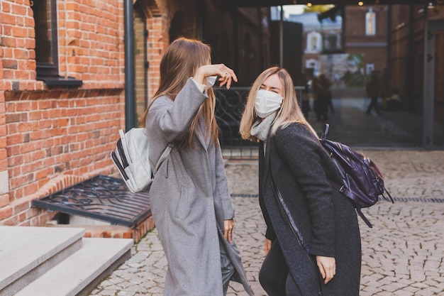 Giovani belle ragazze amiche in maschere mediche che si divertono all'aperto la sera d'autunno in città ridendo