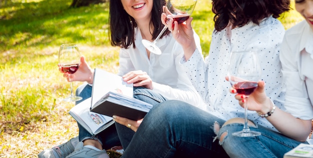 Giovani belle ragazze con bicchiere di vino rosso e libri nel parco.