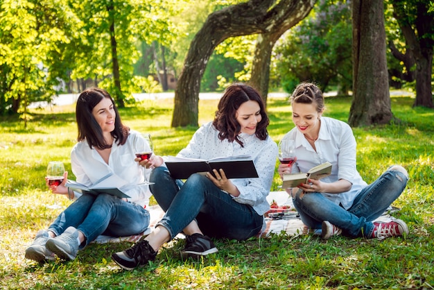 Giovani belle ragazze con bicchiere di vino rosso e libri nel parco.