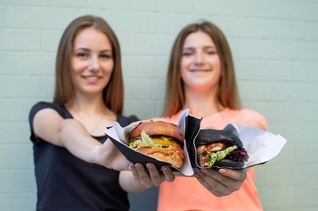 Giovani belle ragazze tengono hamburger e sorridono sono felici quando mangiano fast food