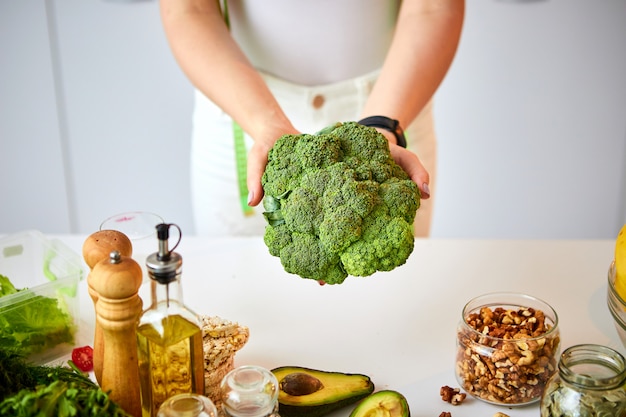 Giovani broccoli felici della tenuta della donna nella bella cucina con gli ingredienti freschi verdi all'interno. Cibo sano e concetto di dieta. Perdere peso