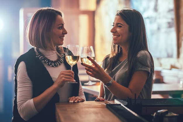 Giovani cari amici sorridenti sono seduti al bar, parlando, brindando e bevendo vino.