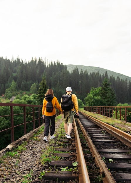 giovani che camminano tenendosi per mano sul binario ferroviario su un viadotto in montagna