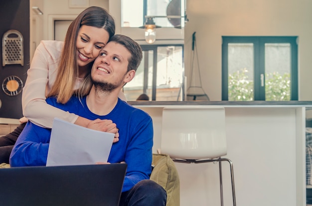 Giovani che studiano da casa con computer portatile, Donna affettuosa guardando il suo ragazzo lavorando al computer portatile a casa