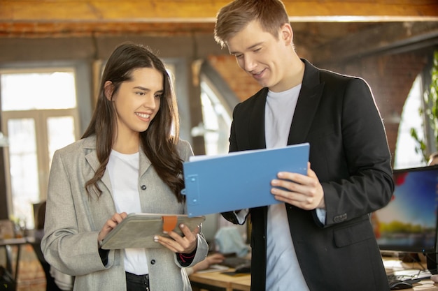 Giovani colleghi caucasici che lavorano insieme in un ufficio utilizzando dispositivi e gadget moderni