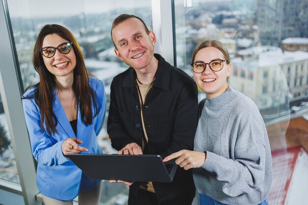 Giovani colleghi studenti che lavorano su un nuovo progetto in piedi vicino alle finestre in un moderno spazio di lavoro vicino alla finestra Gli uomini d'affari lavorano a distanza